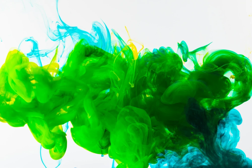 A macro photograph of green and blue ink spreading in water.
